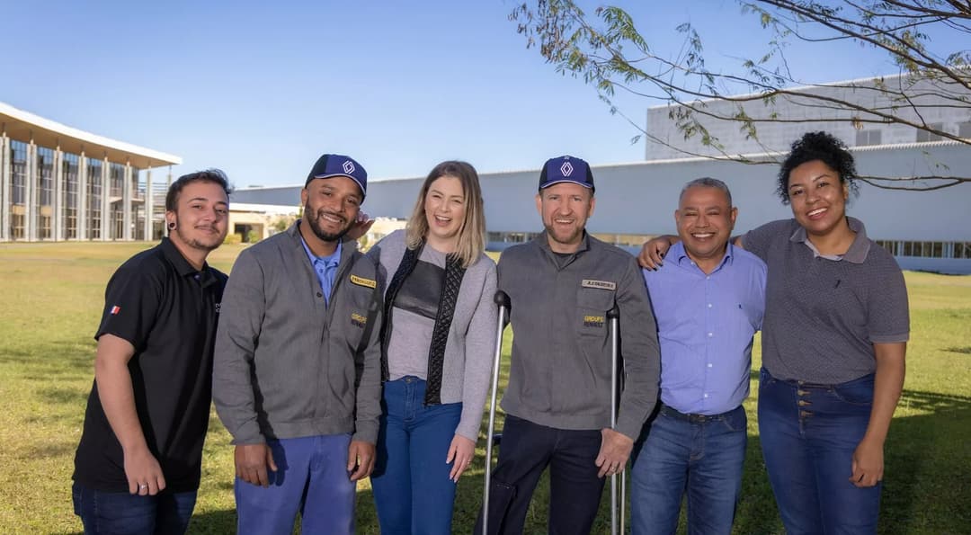 Funcionários da Renault do Brasil sorrindo em frente à fábrica, representando diversidade e inclusão no ambiente corporativo.